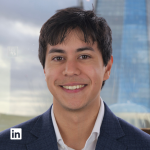 Smiling man in a navy blazer and white shirt, posing for a professional headshot with a blurred cityscape background (LinkedIn logo visible).